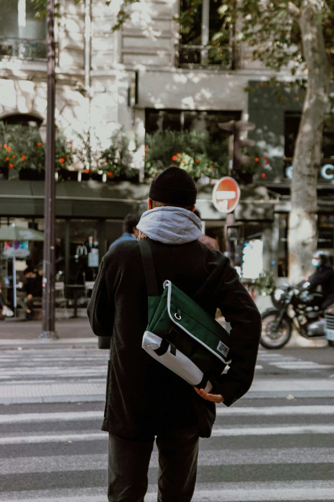 person in black jacket and white knit cap walking on sidewalk during daytime